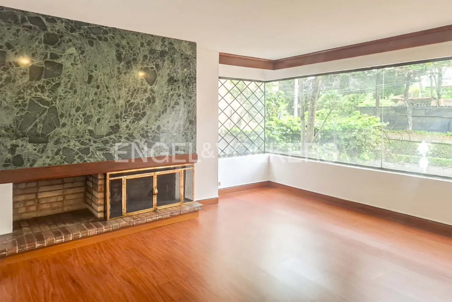 Living room with wood floors, a large green marble fireplace, and a corner window overlooking a garden.