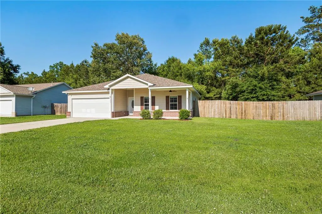 A single-story beige house with a white garage door and a large green lawn.