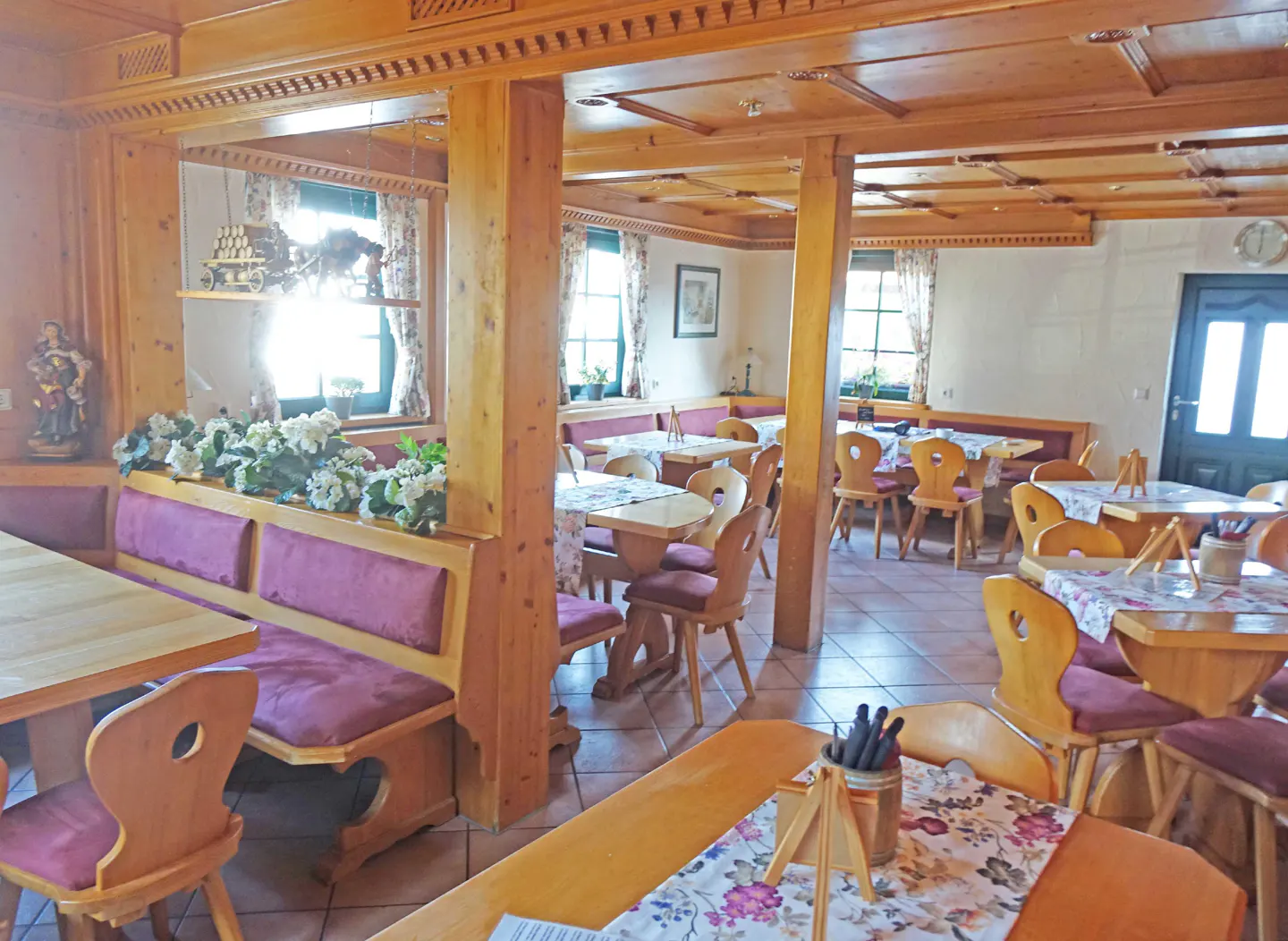 Interior of a restaurant with wooden tables, chairs, and booths with purple cushions. Floral tablecloths and decorations add charm.