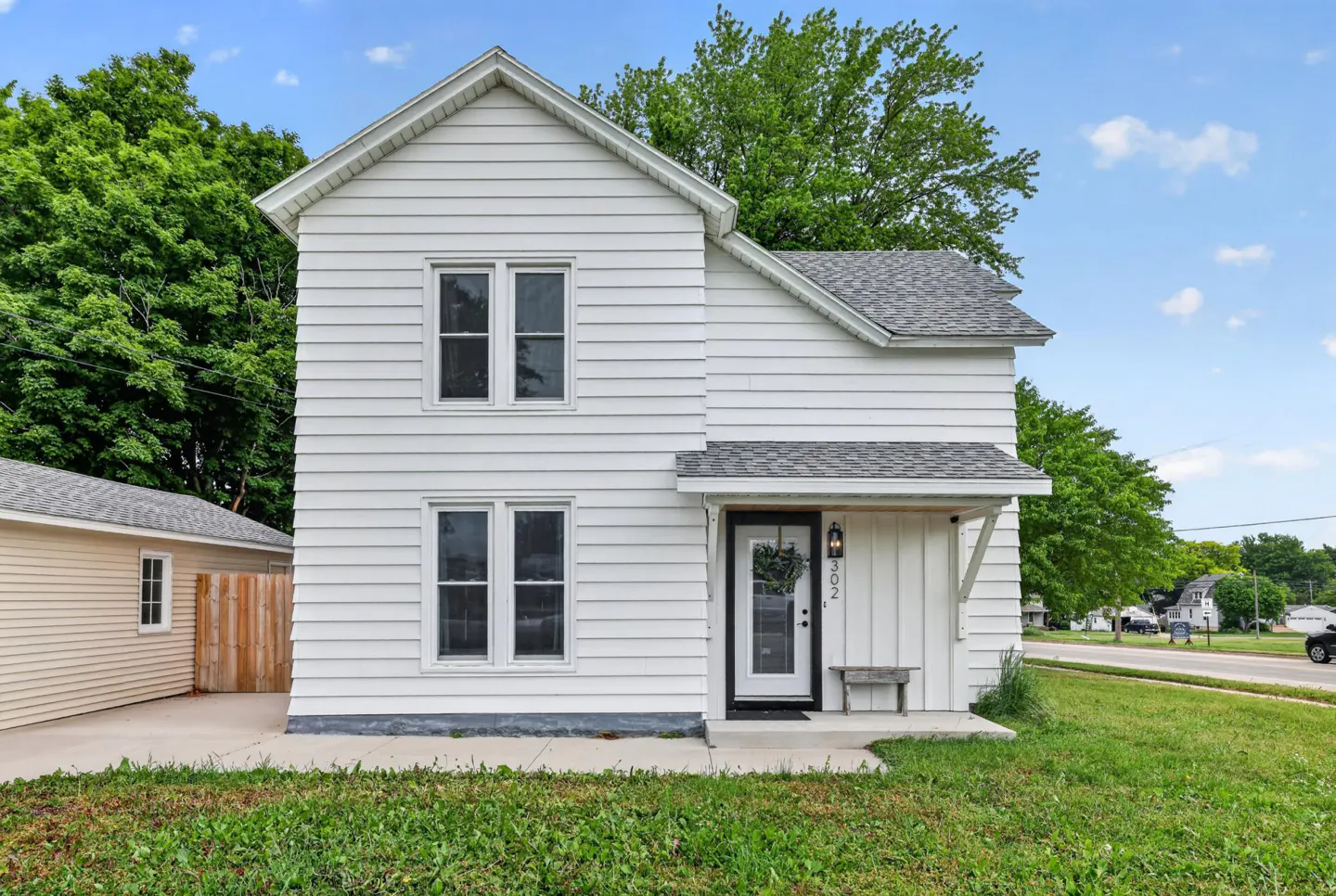Two-story white house with horizontal siding, a gray shingled roof, and a small front porch with a wooden bench.