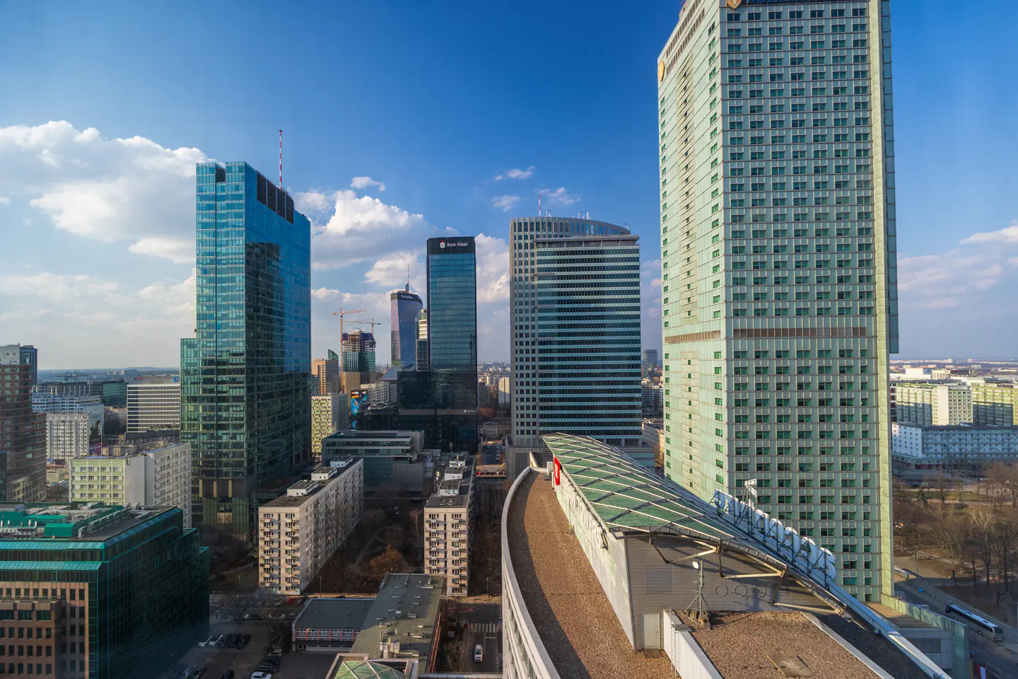 Cityscape view of Warsaw, Poland, featuring modern skyscrapers against a blue sky with scattered clouds.