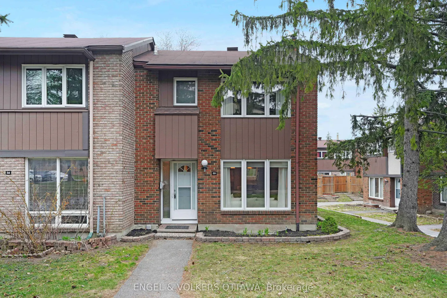 Exterior view of a two-story brick townhouse with a white front door and a small garden.