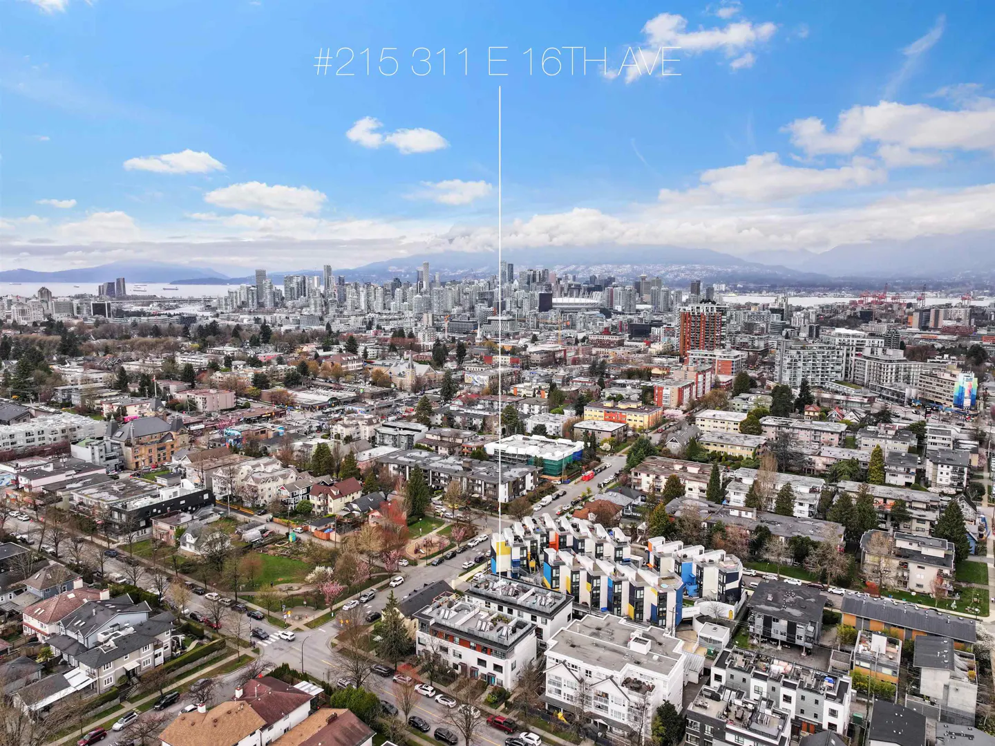 Aerial view of #215 311 E 16th Ave, Vancouver, with colorful modern townhouses in the foreground and city skyline in the background.