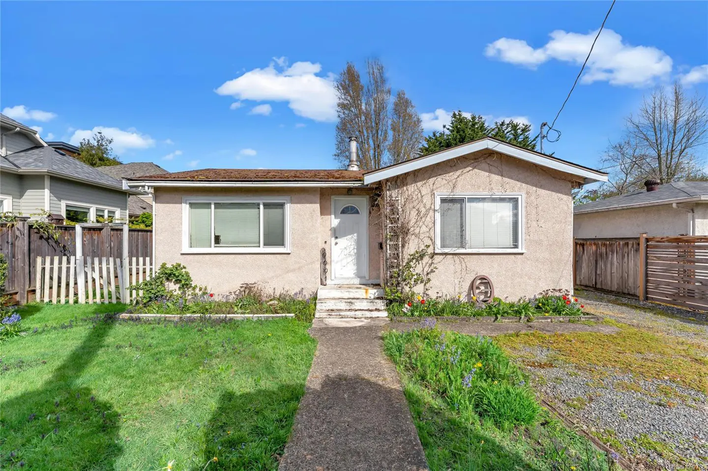 A tan stucco house with a white door and trim, a concrete walkway, and a green lawn under a blue sky.