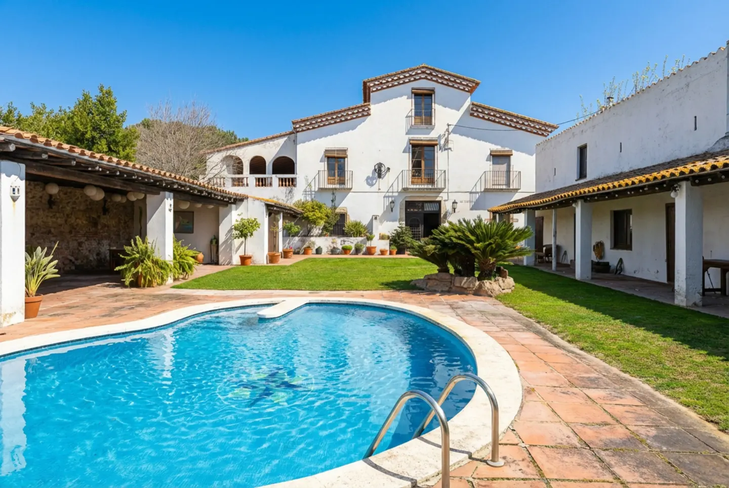A white two-story house with a red tile roof overlooks a blue kidney-shaped pool with a brick patio.