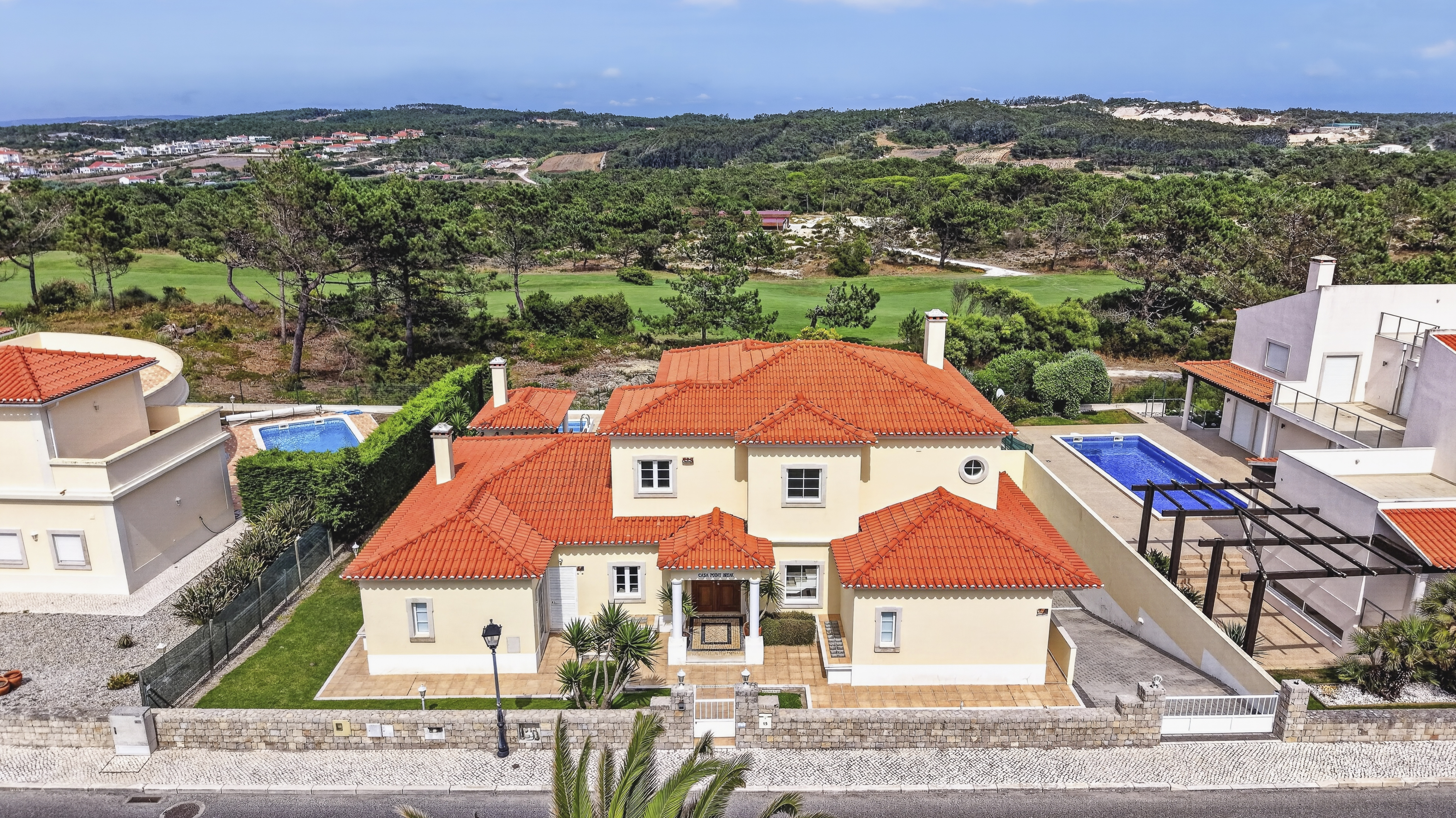 Aerial view of a cream-colored villa with a red tile roof, private pool, and scenic golf course backdrop.