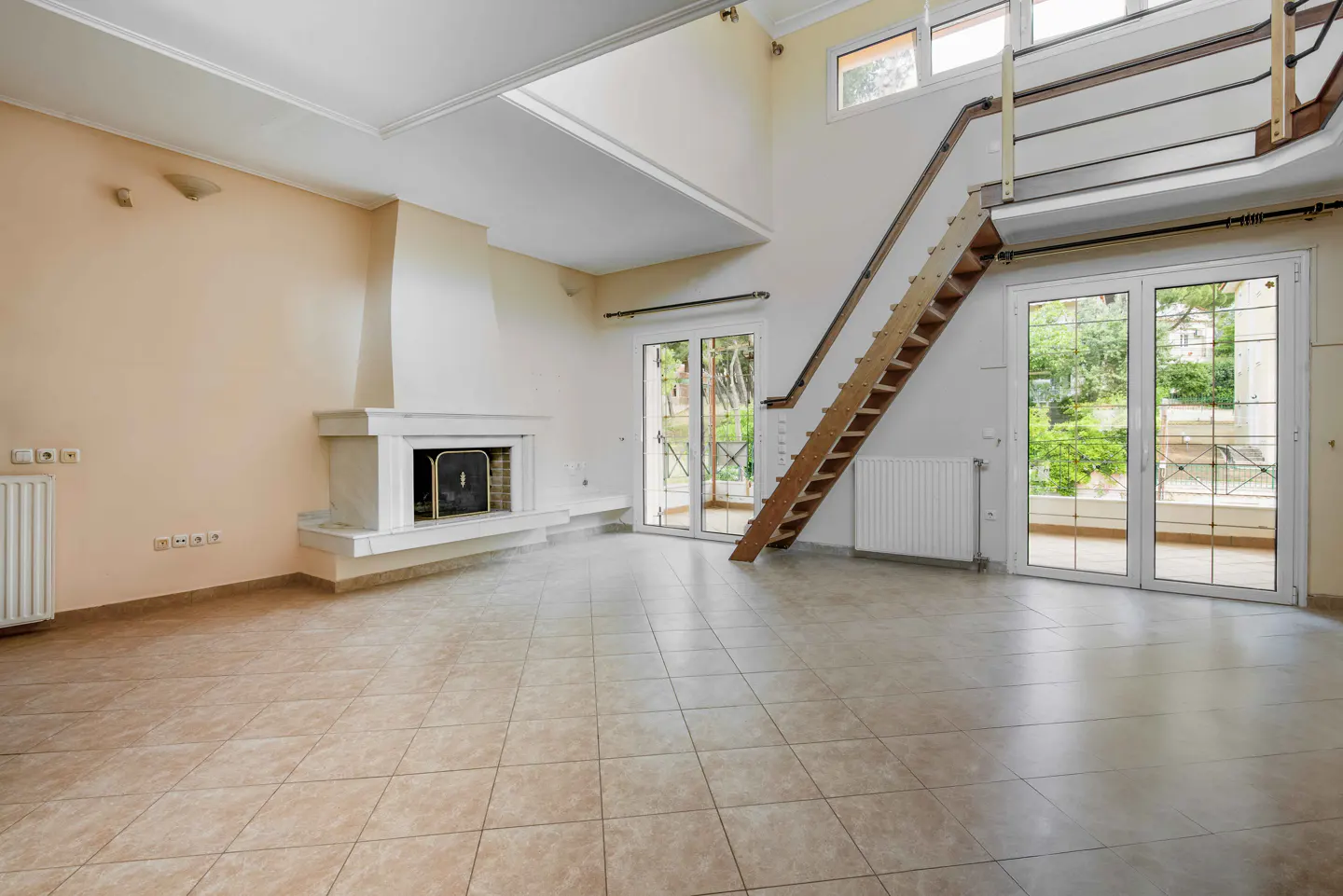Spacious living room with tile floors, a white fireplace, and a wooden staircase leading to an upper loft area.