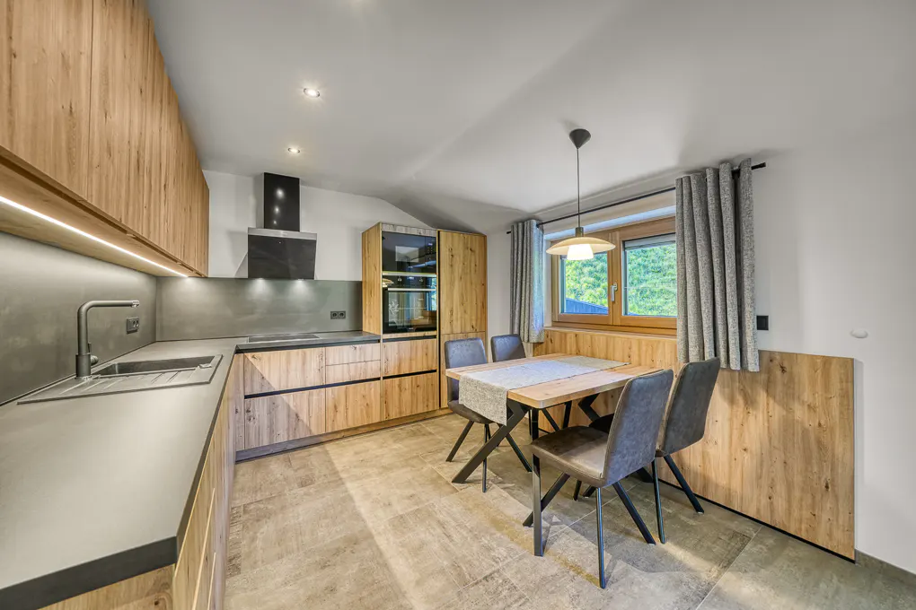 A modern kitchen with wood cabinets, gray countertops, and a dining table with four chairs.