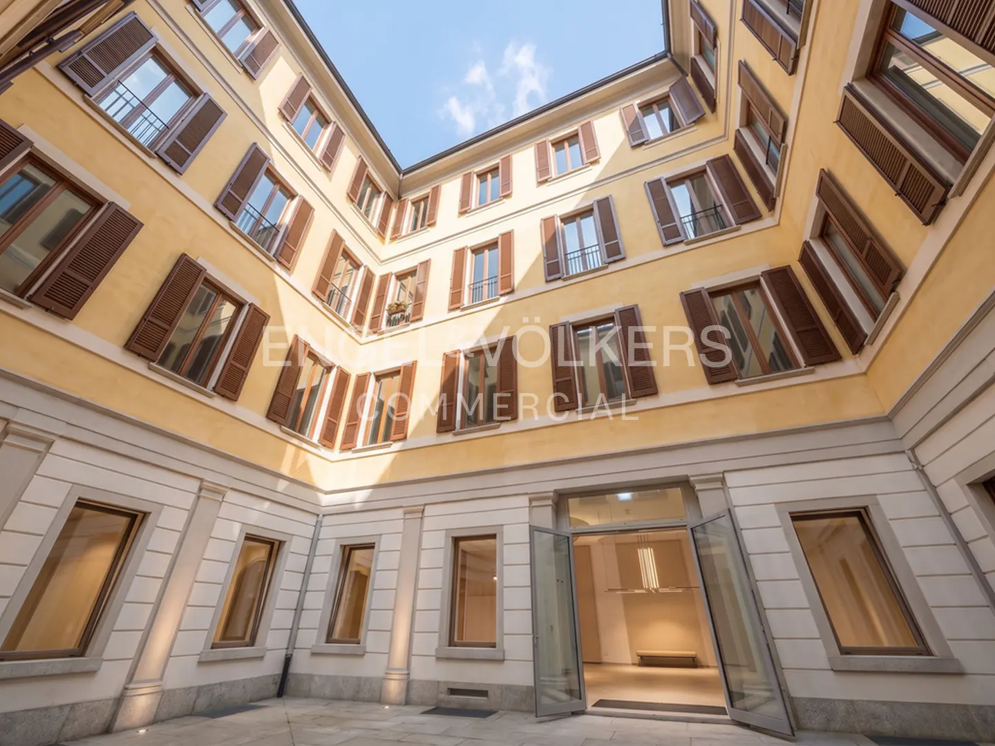 Courtyard view of a yellow building with brown shutters and a glass door entrance.