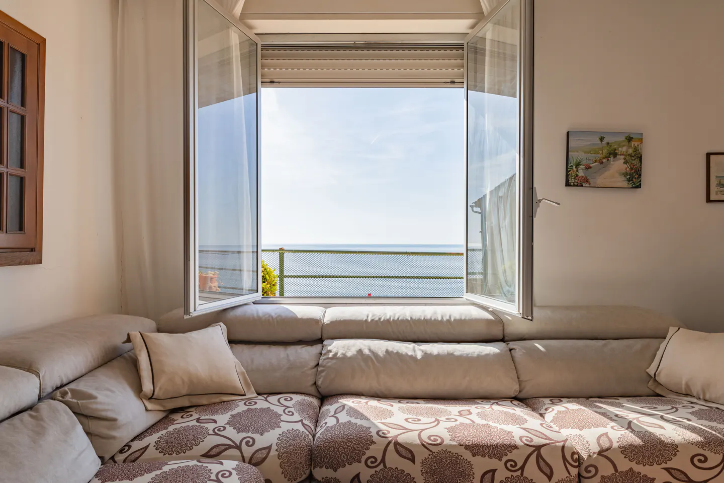 Living room with a floral sofa and open window view of the ocean.