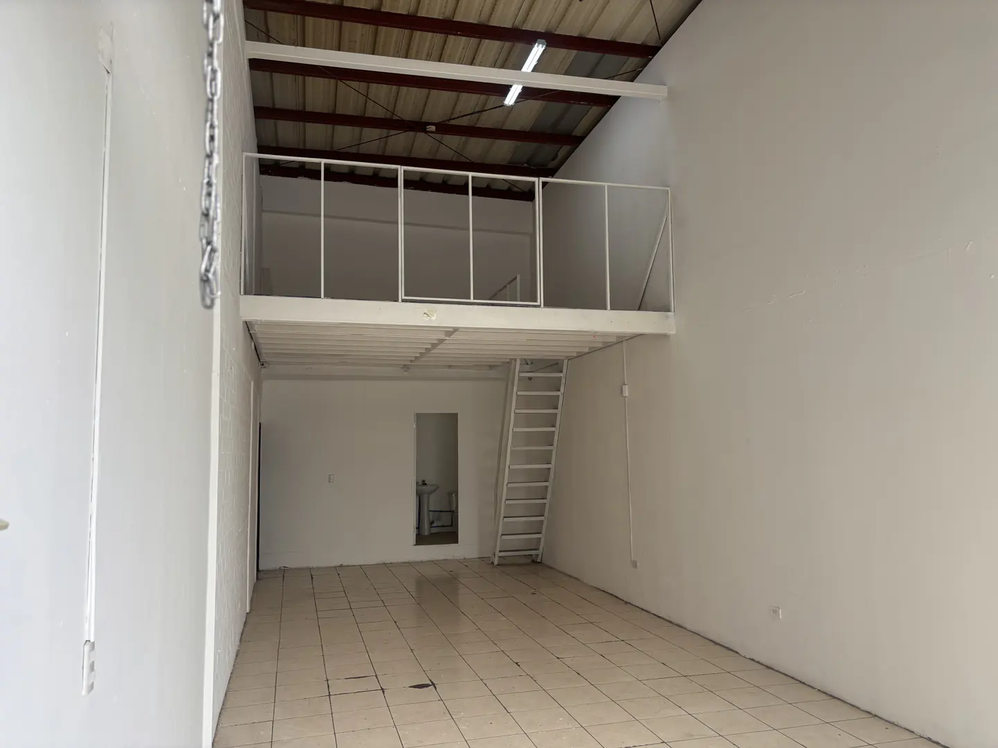 Interior of a commercial space with white walls, tile floors, and a white metal mezzanine with a ladder.