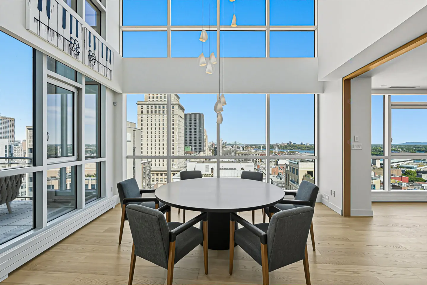 Bright, modern dining room with a round table, gray chairs, and floor-to-ceiling windows offering a city view.