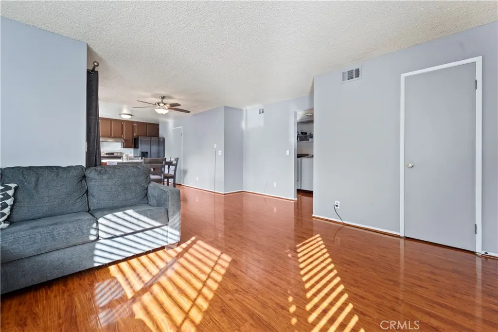 Living room with gray sofa, wood floors, and light gray walls. Kitchen and dining area are visible in the background.
