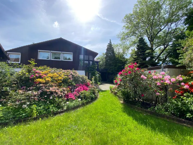 A brown house with a green lawn and colorful flowers in the front yard on a sunny day.