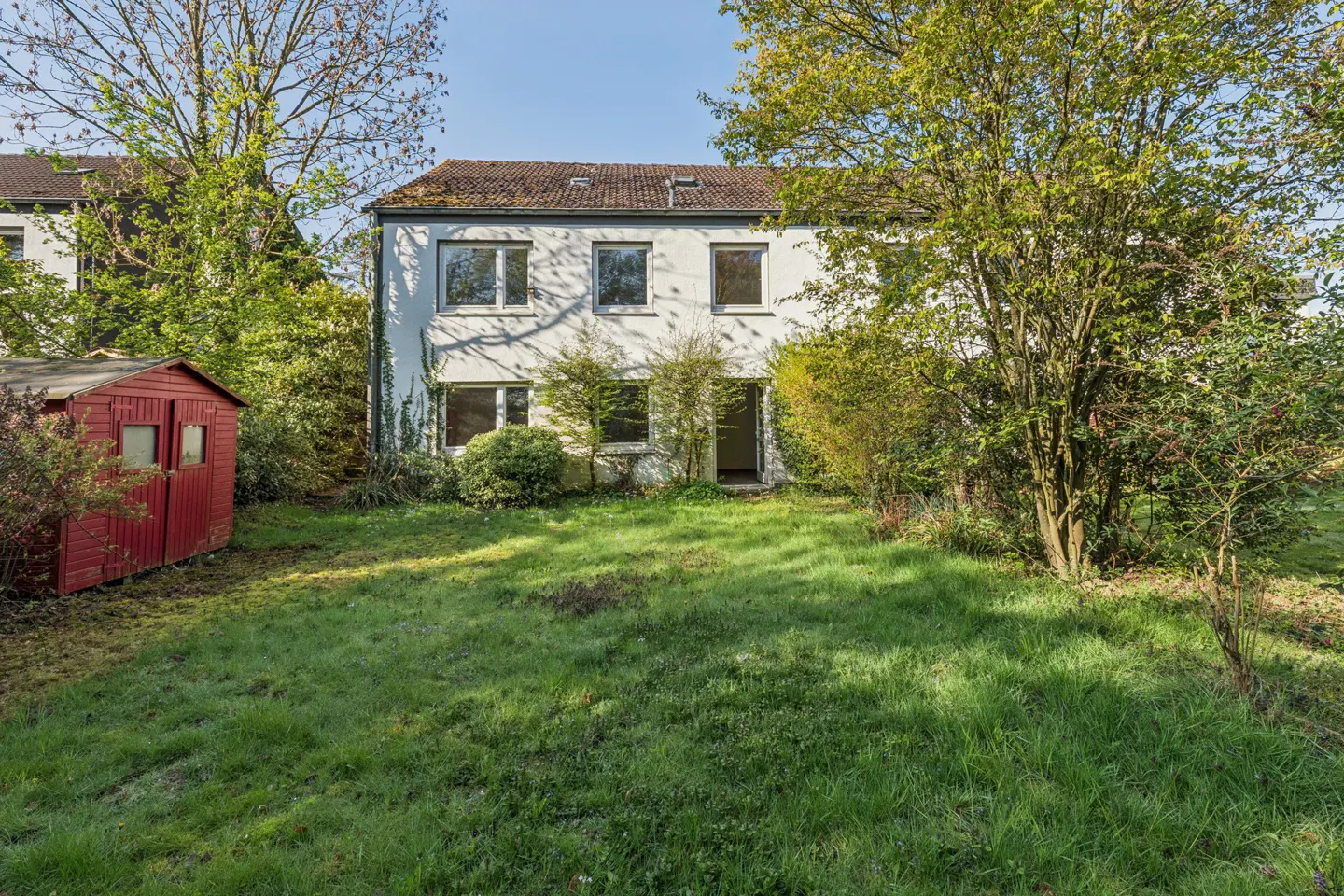 Two-story white house with a red shed in the yard, surrounded by green trees and grass.