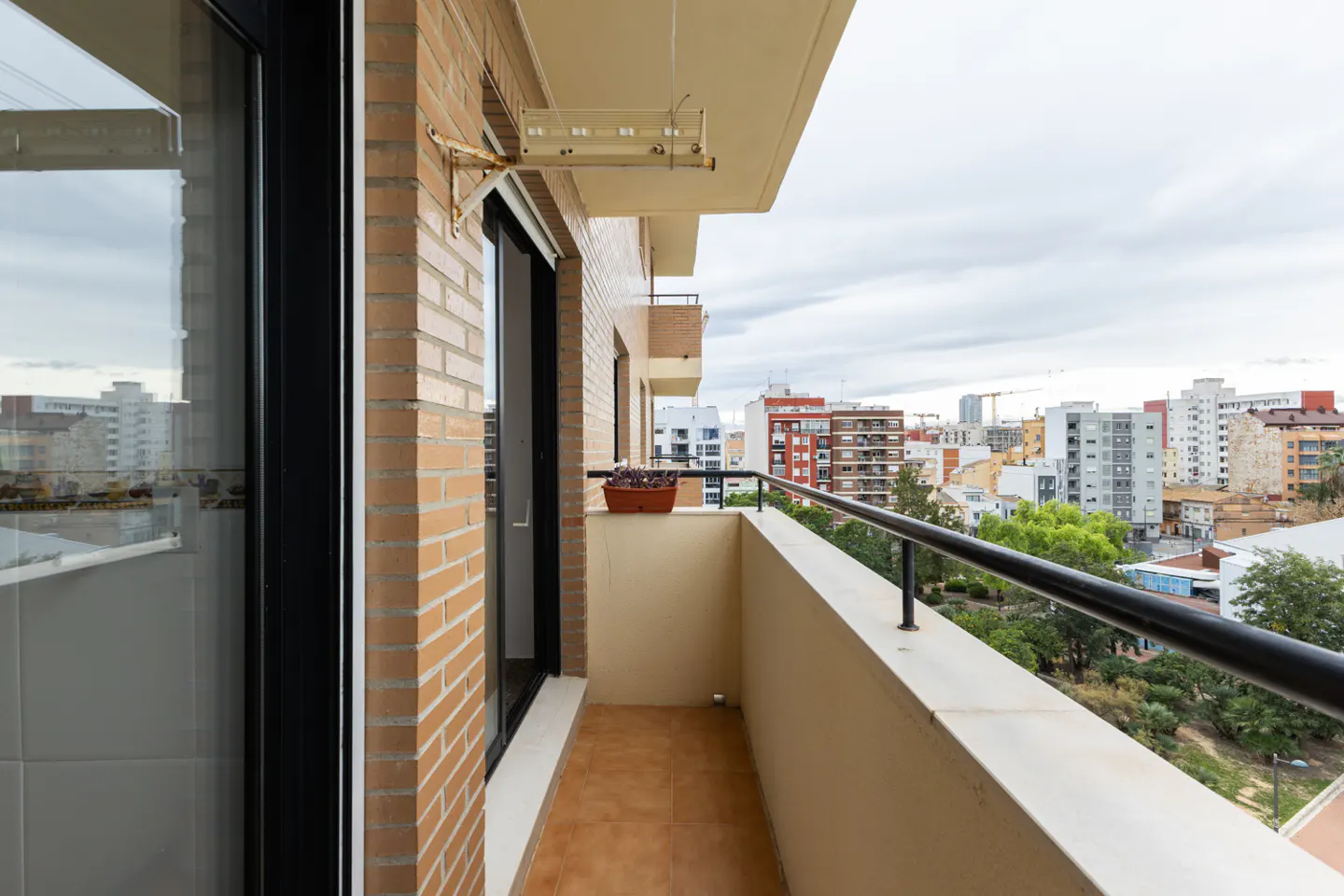 A balcony with a black railing overlooks a city. A flower pot sits on the balcony wall. The building is brick.