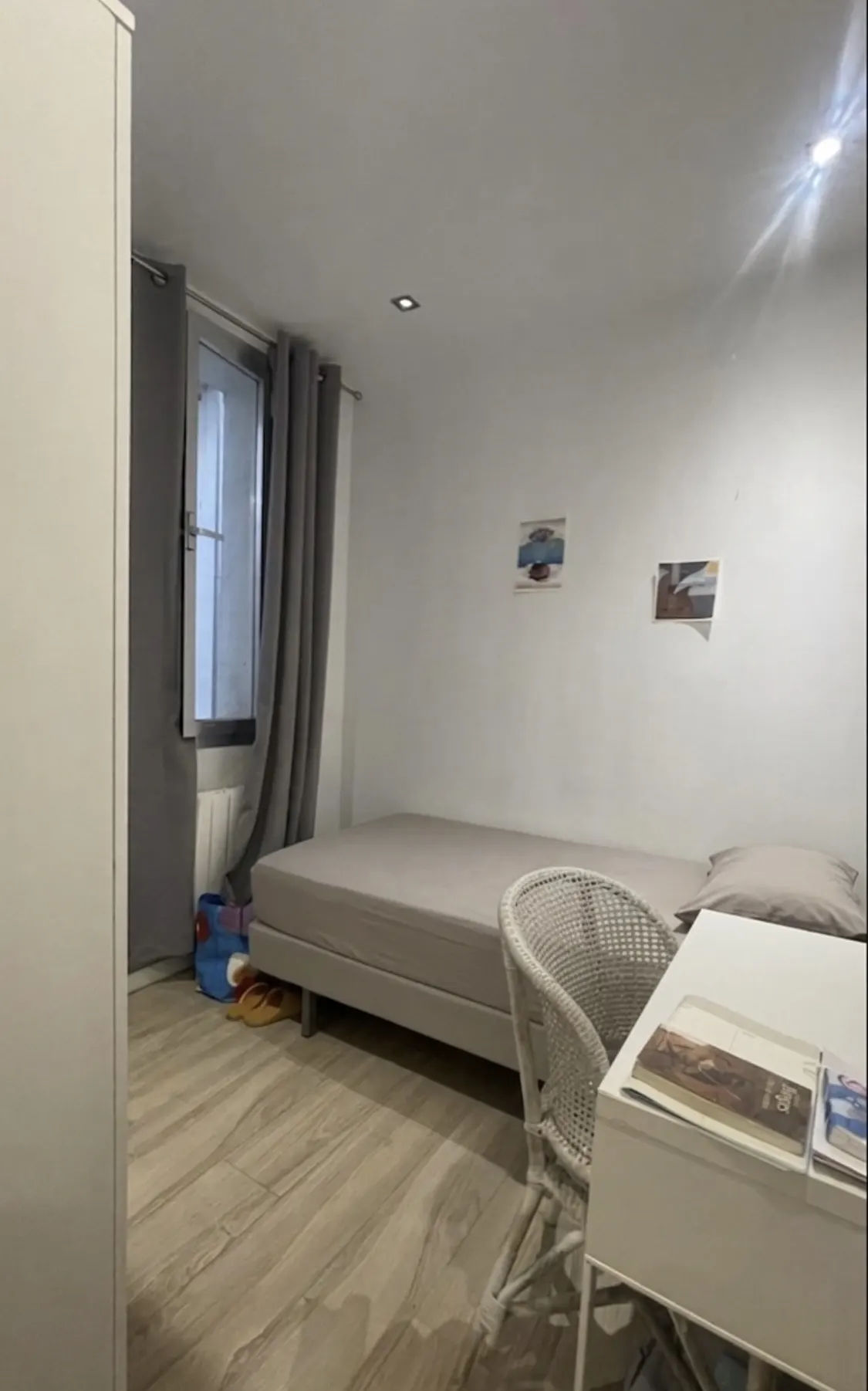 A bedroom with a single bed, white walls, a desk, and a window with gray curtains.
