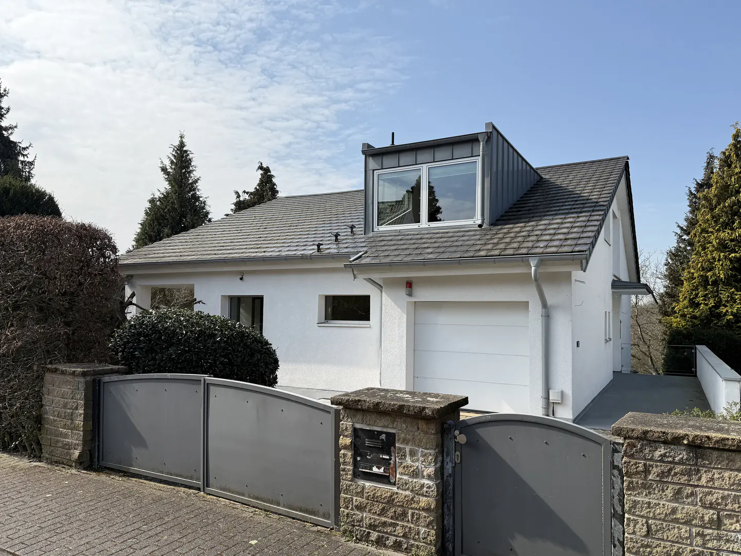 A white, one-story house with a gray roof and a gray metal gate in front.