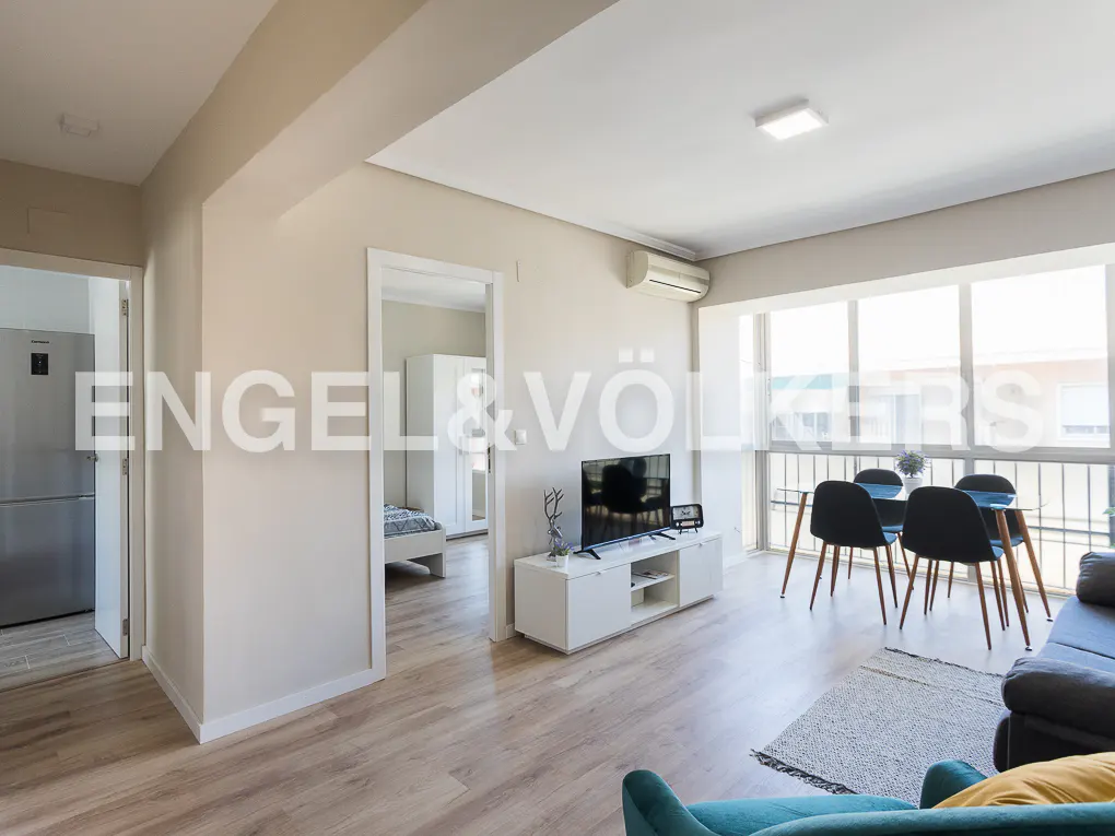 Bright living room with light wood floors, a white media console, dining area, and a view into a bedroom.