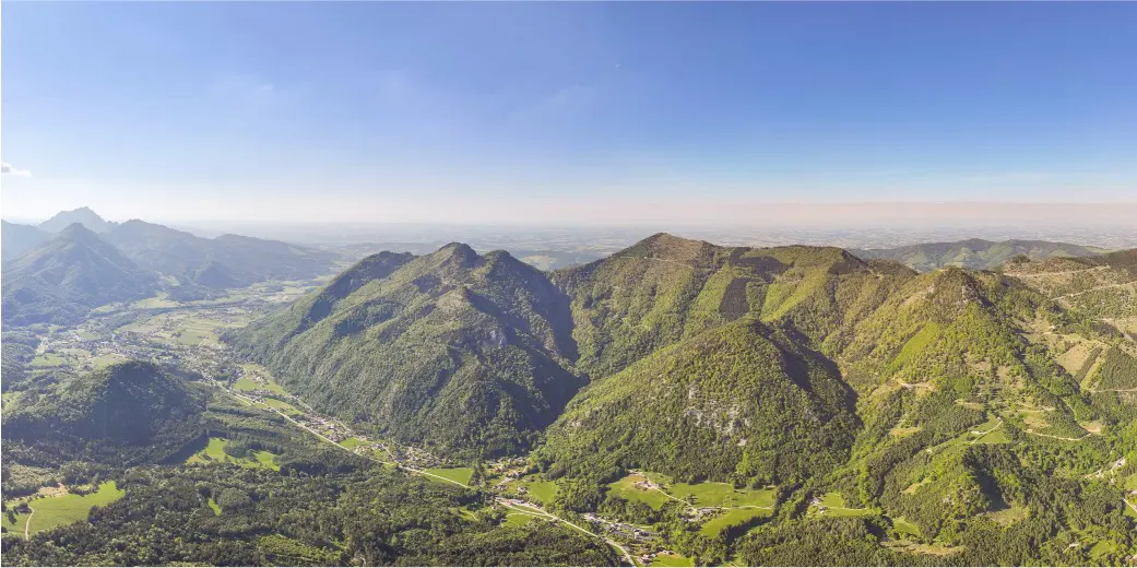 Scenic aerial view of green, tree-covered mountains under a clear blue sky, with a small village nestled in the valley below.