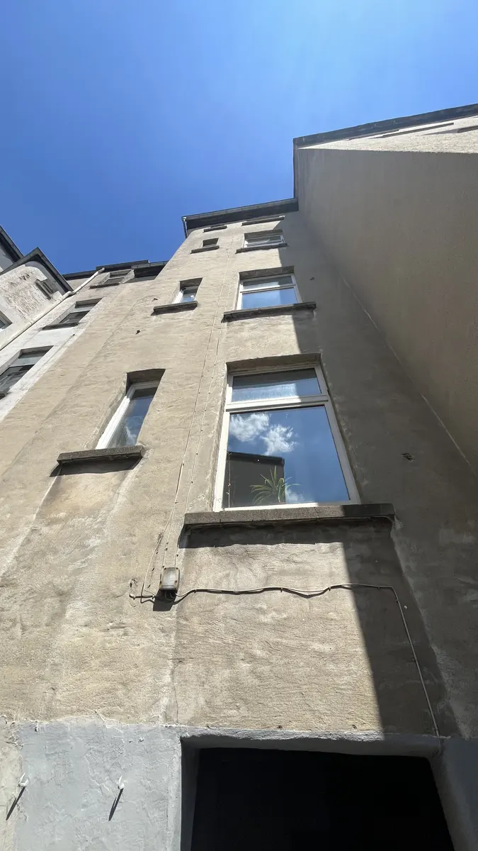 Looking up at a tall, beige apartment building with white-framed windows reflecting the blue sky.