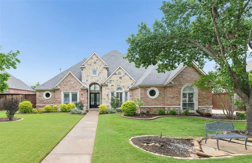 Two-story home with brick and stone exterior, gray roof, and green lawn under a blue sky. A sidewalk leads to the front door.