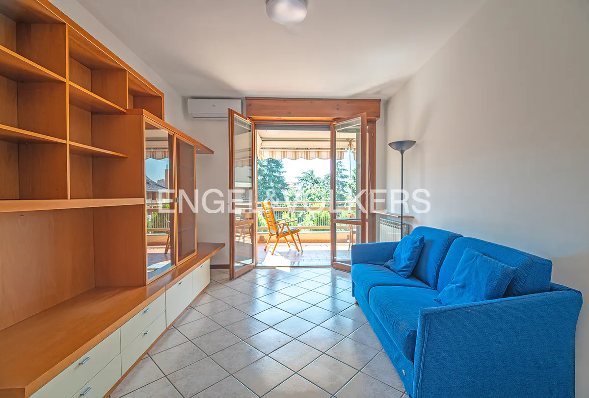 Living room with a blue sofa, wooden shelves, and an open balcony door with a chair.