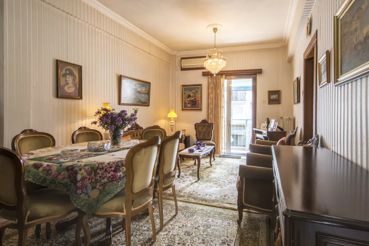 A dining room with a table, chairs, and floral tablecloth. Paintings hang on the striped walls. A chandelier hangs from the ceiling.