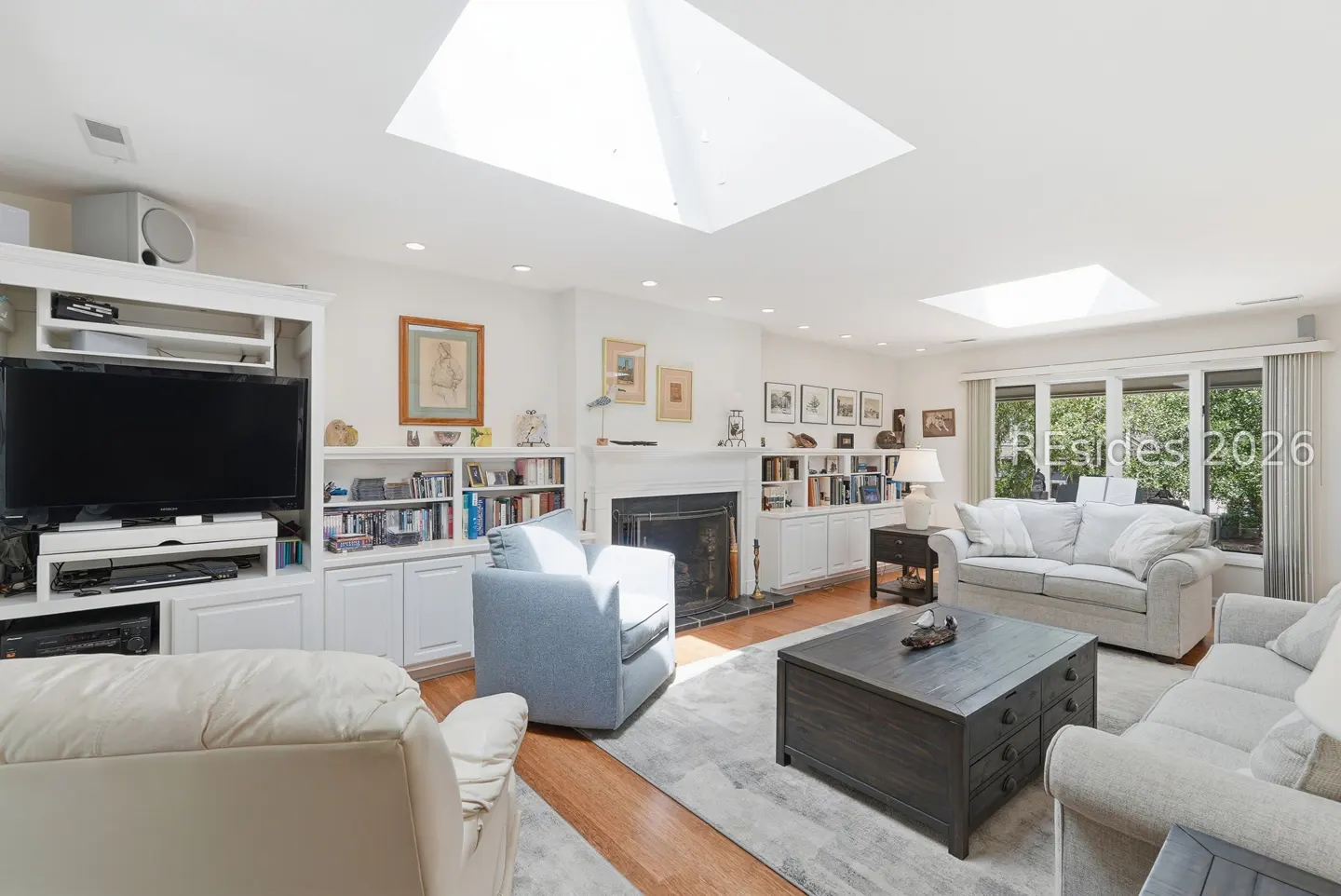 Bright living room with skylights, built-in shelves, fireplace, and light-colored sofas and chairs.