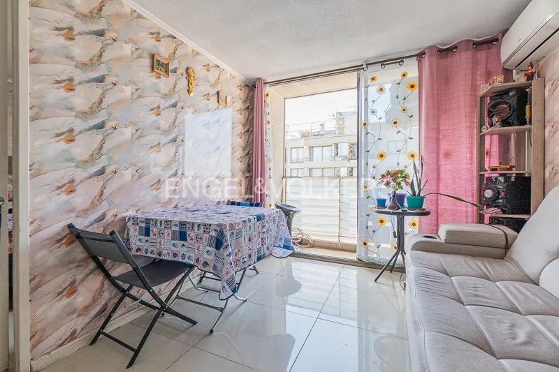 A bright living room with a table, chairs, and a white sofa. Pink curtains frame a balcony with a city view. The wall has a marble-like pattern.