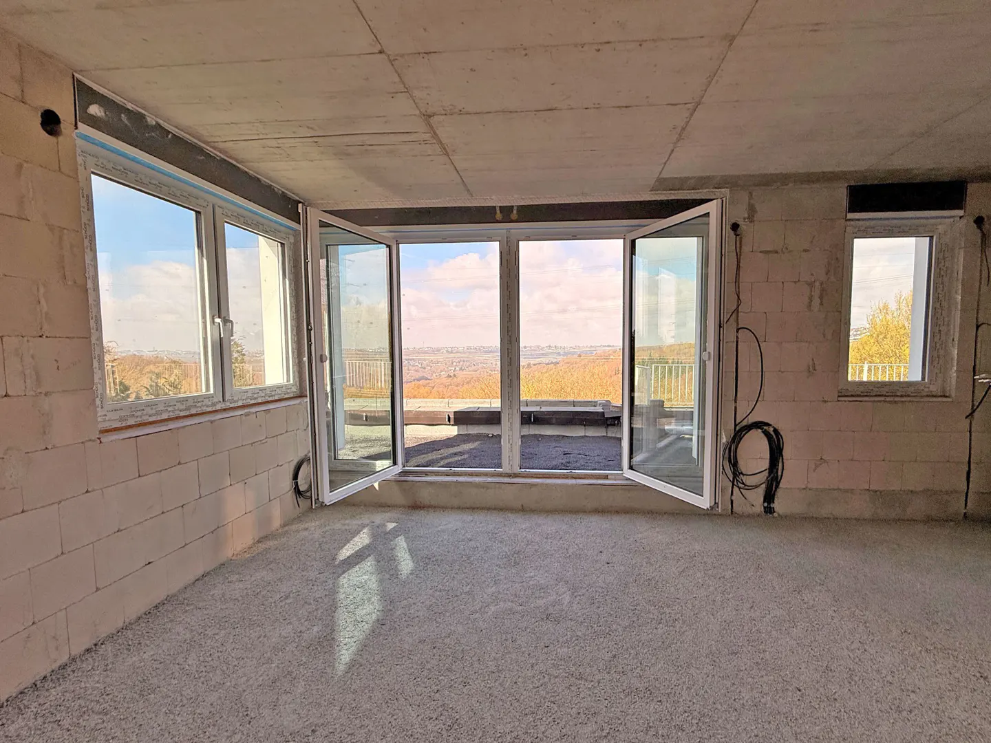 Unfinished room with white brick walls, concrete floor and ceiling, and open white frame doors with a view of trees and city.