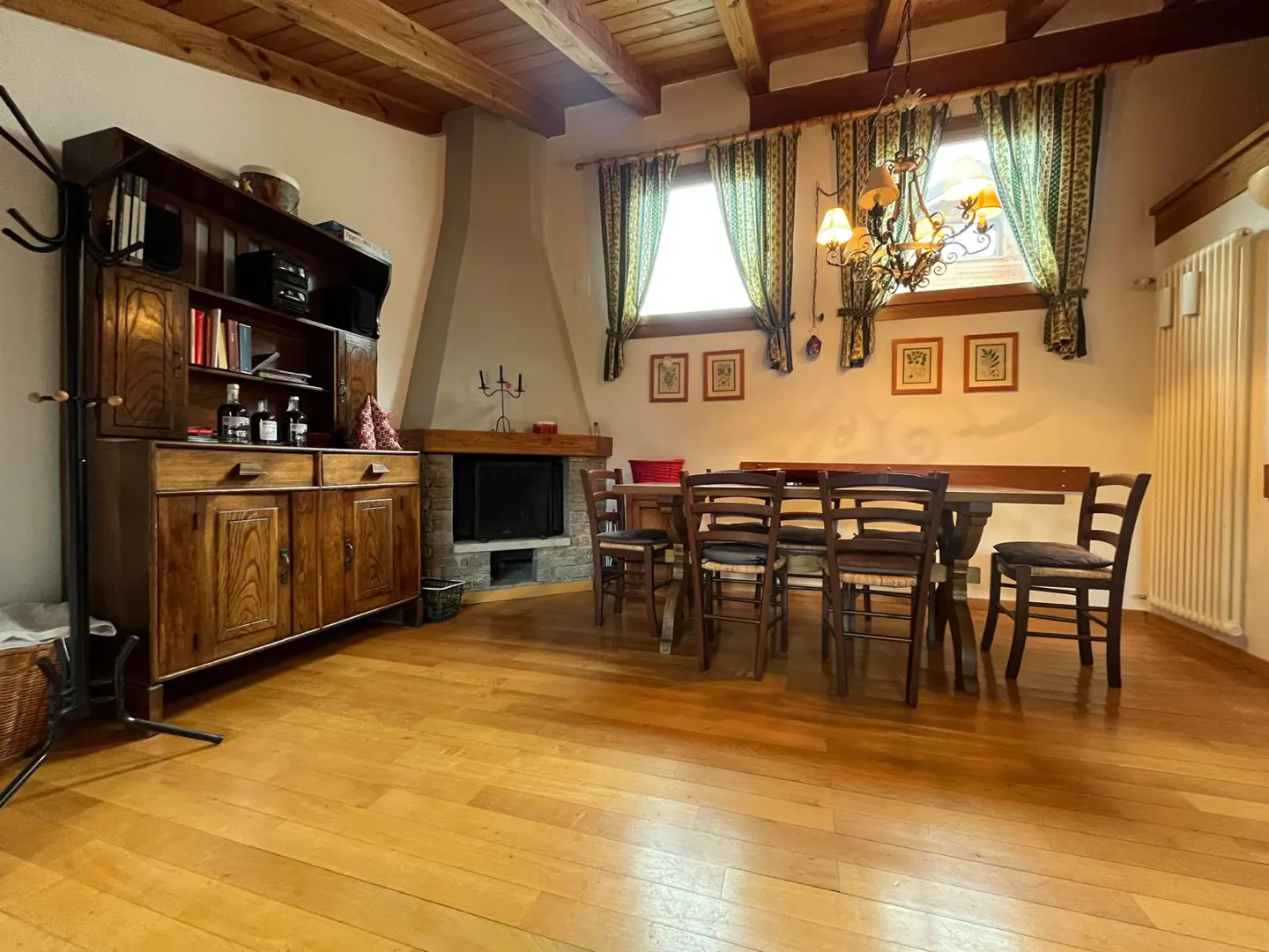 Rustic dining room with wooden floors, a stone fireplace, a large hutch, and a table with four chairs under a chandelier.