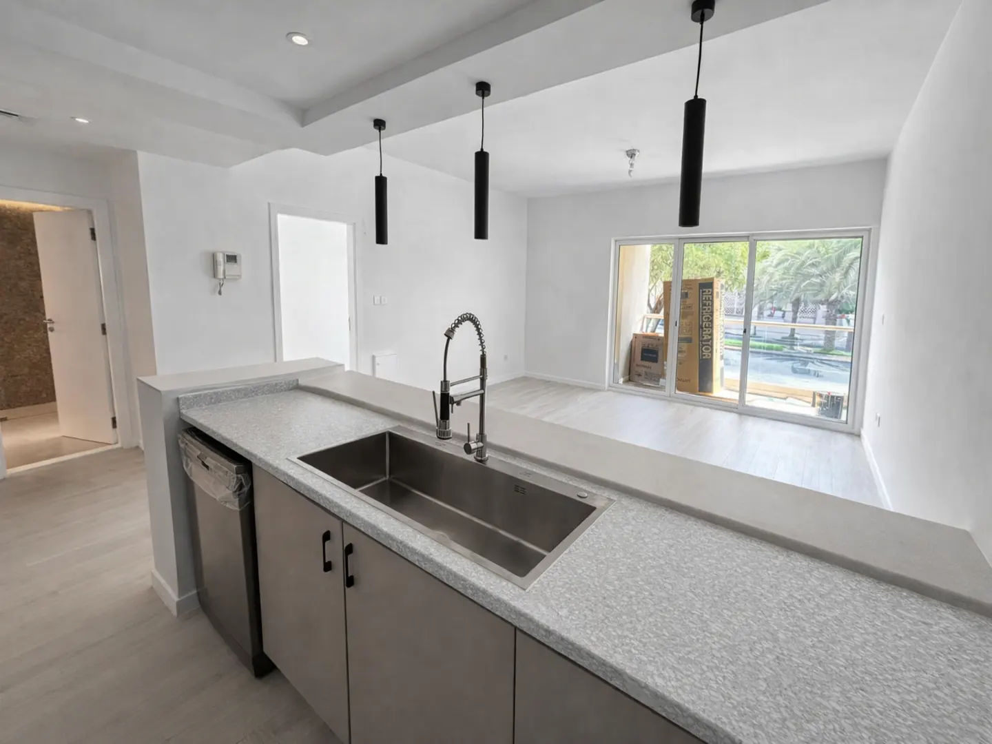 Modern kitchen with grey cabinets, speckled countertops, stainless steel sink, and three black pendant lights.