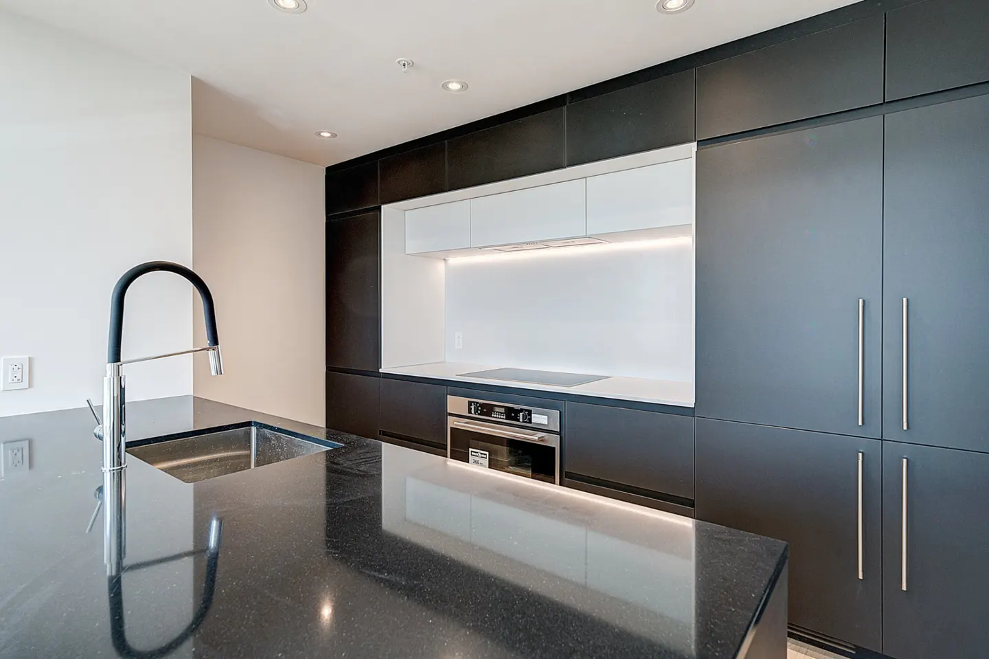 Modern kitchen with black granite island, stainless steel sink and faucet, black and white cabinets, and stainless steel oven.