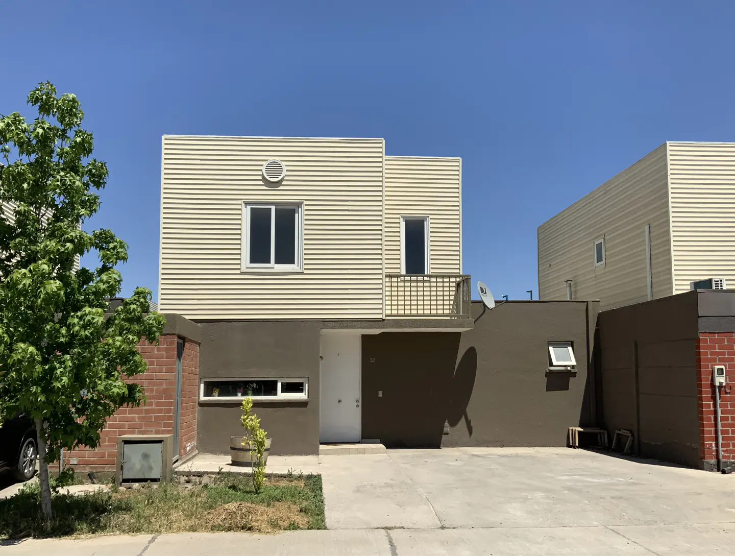 Two-story house with beige siding and a brown stucco base under a clear blue sky. A tree is on the left.