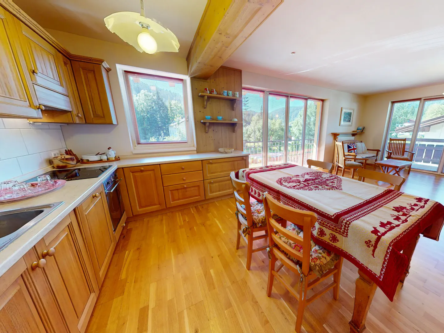 A bright kitchen and dining area with wooden cabinets, a table with a red and white tablecloth, and a view of mountains.