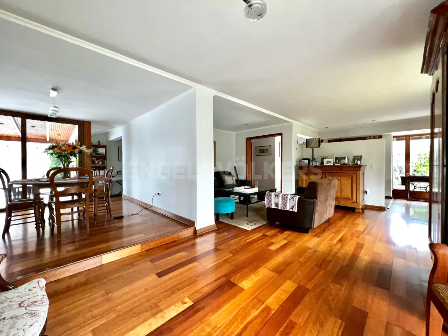 Open-plan living area with hardwood floors, a dining set on a raised platform, and a cozy lounge with a brown armchair.