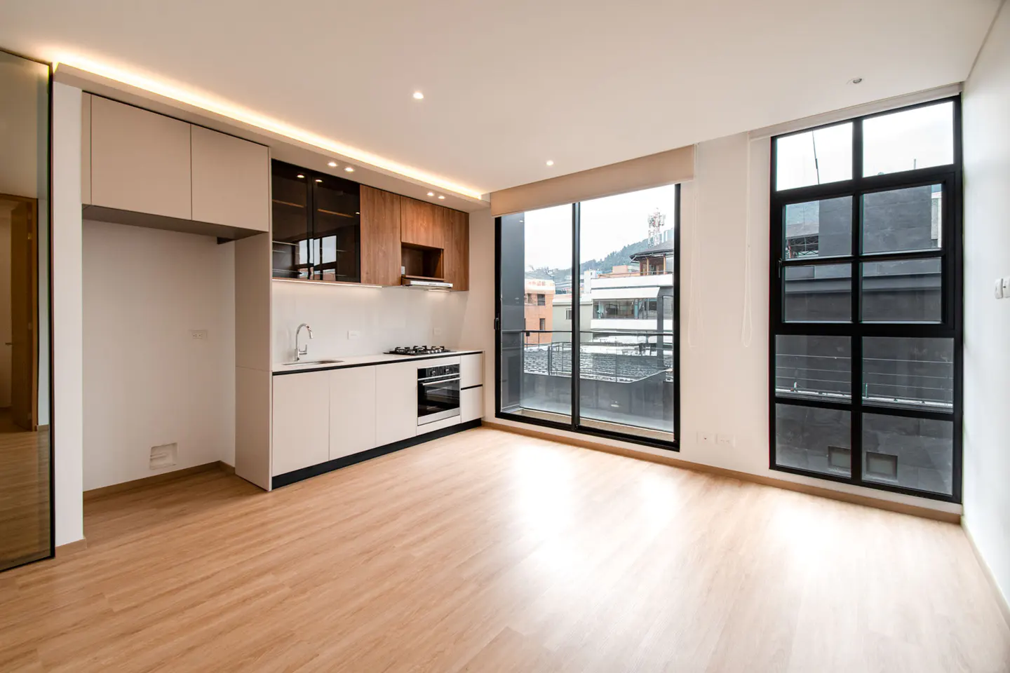 Bright, modern kitchen with light wood floors, white cabinets, and black-framed windows overlooking a cityscape.