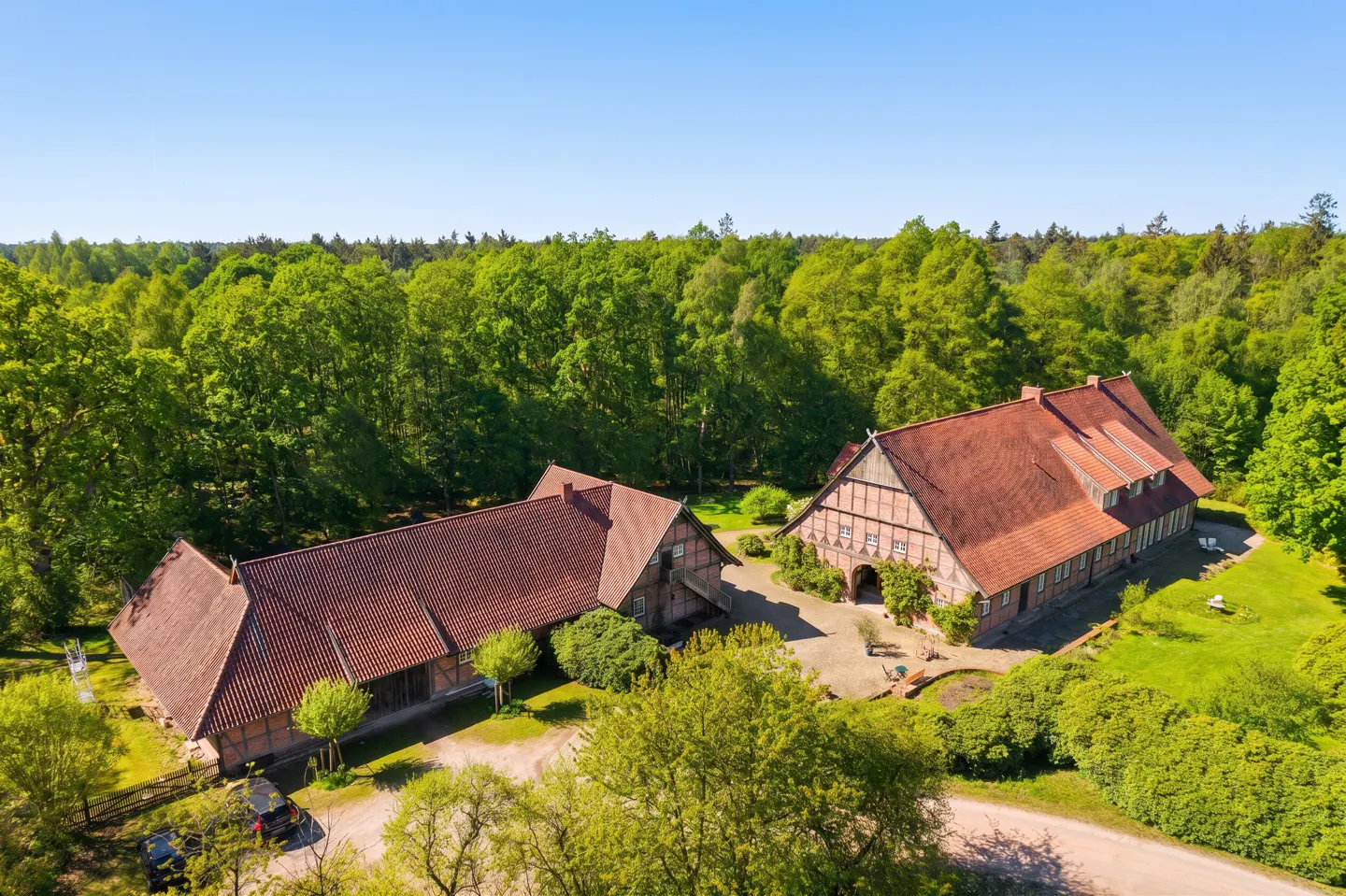 Aerial view of two traditional timber-framed farmhouses with red tile roofs surrounded by lush green trees and a lawn.