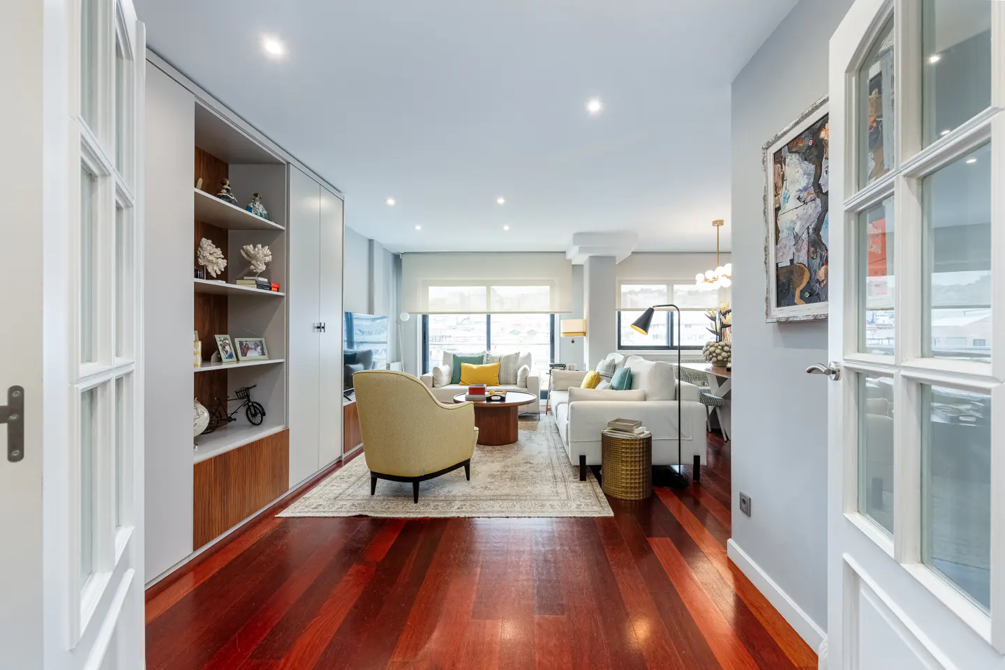 Open doorway view of a modern living room with hardwood floors, white sofas, and built-in shelving.