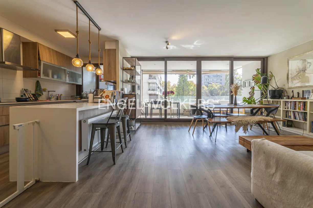 Open-concept living space with kitchen island, dining table, and balcony access. Wood floors and natural light.