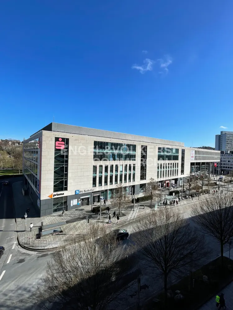 Exterior shot of a modern, multi-story commercial building with large windows and the Engel & Volkers logo on a sunny day.