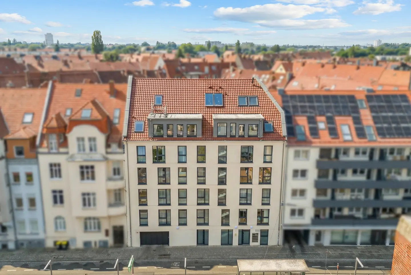 A cream-colored apartment building with a red tile roof and many windows, surrounded by other buildings with red roofs.