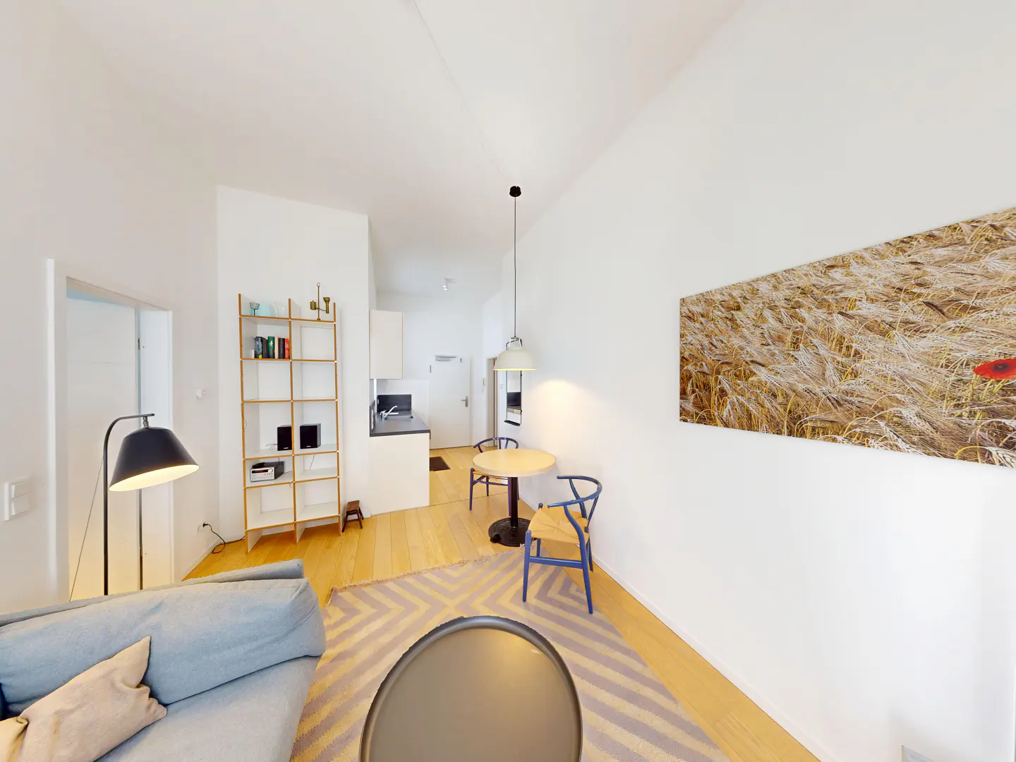Bright apartment interior with a blue sofa, round table, and wheat field art on a white wall.