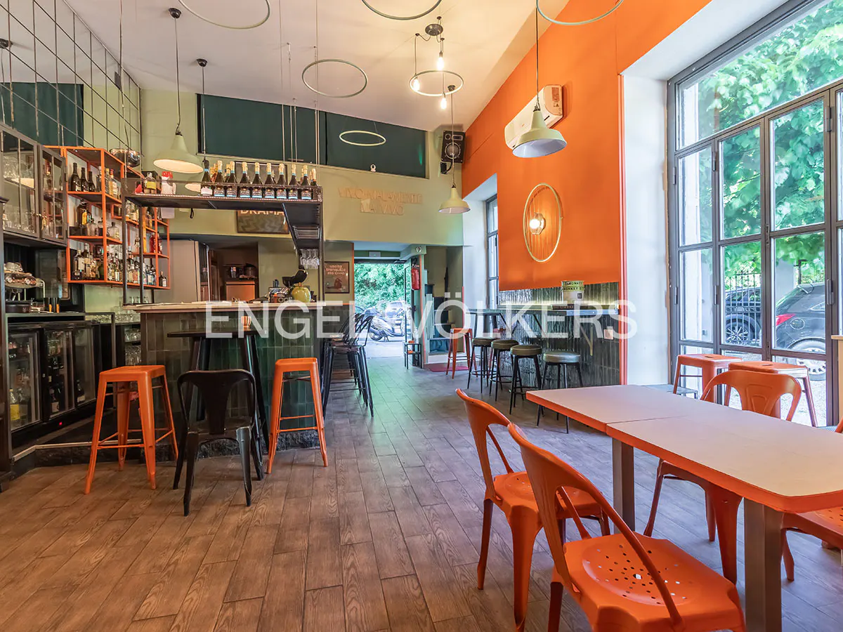 Interior view of a bar with orange walls, wooden floors, tables, chairs, and a bar with stools.