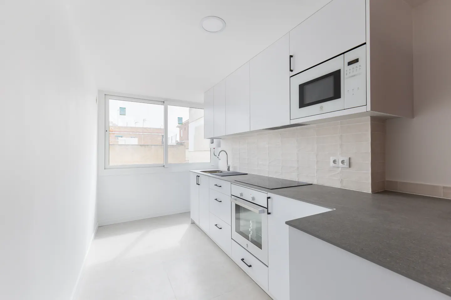 Bright, modern kitchen with white cabinets, gray countertops, and stainless steel appliances. A window provides natural light.