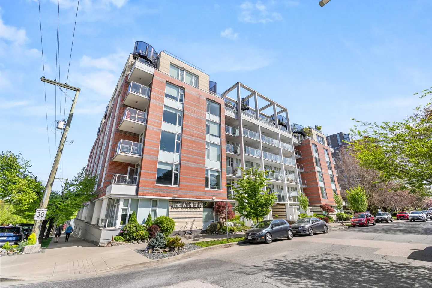 Exterior view of "The Wuhlsen" condos, a multi-story brick and white building with balconies, cars parked on the street.