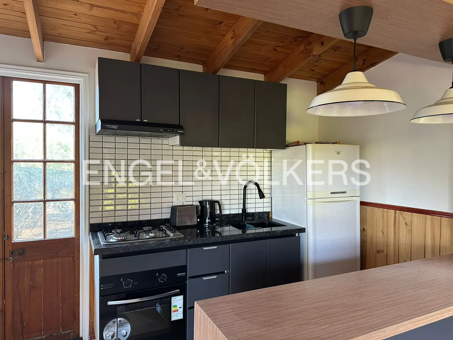 A kitchen with black cabinets, a white fridge, and a wooden ceiling.