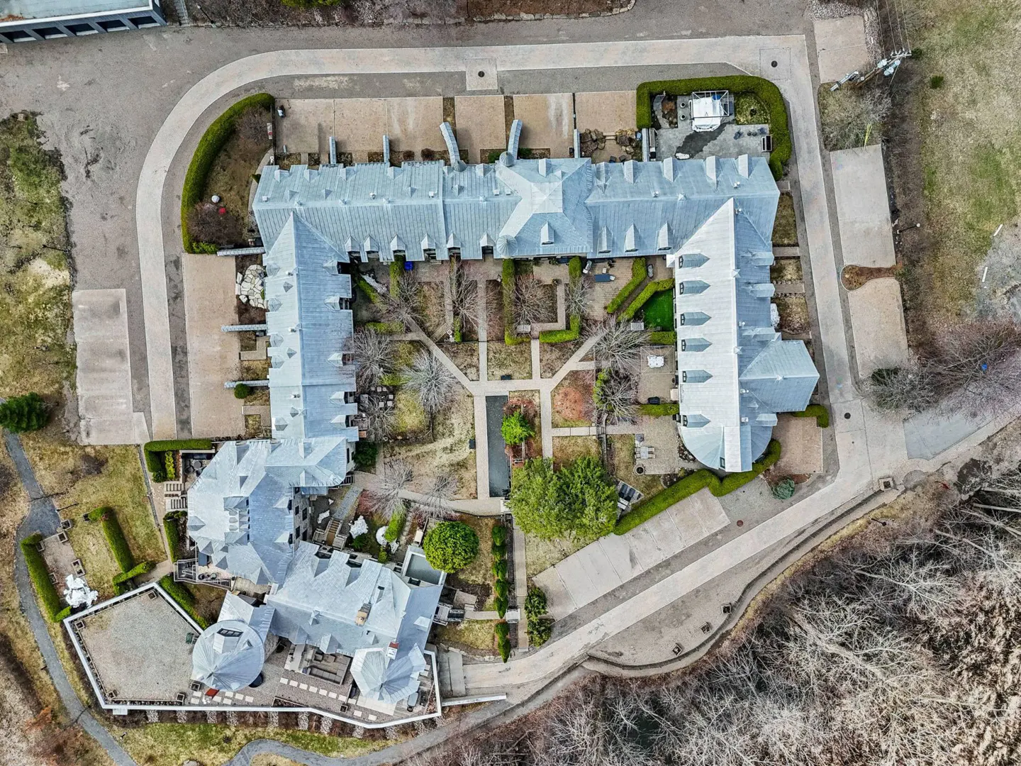 Aerial view of a large, gray-roofed building with a central courtyard garden and surrounding green lawns.