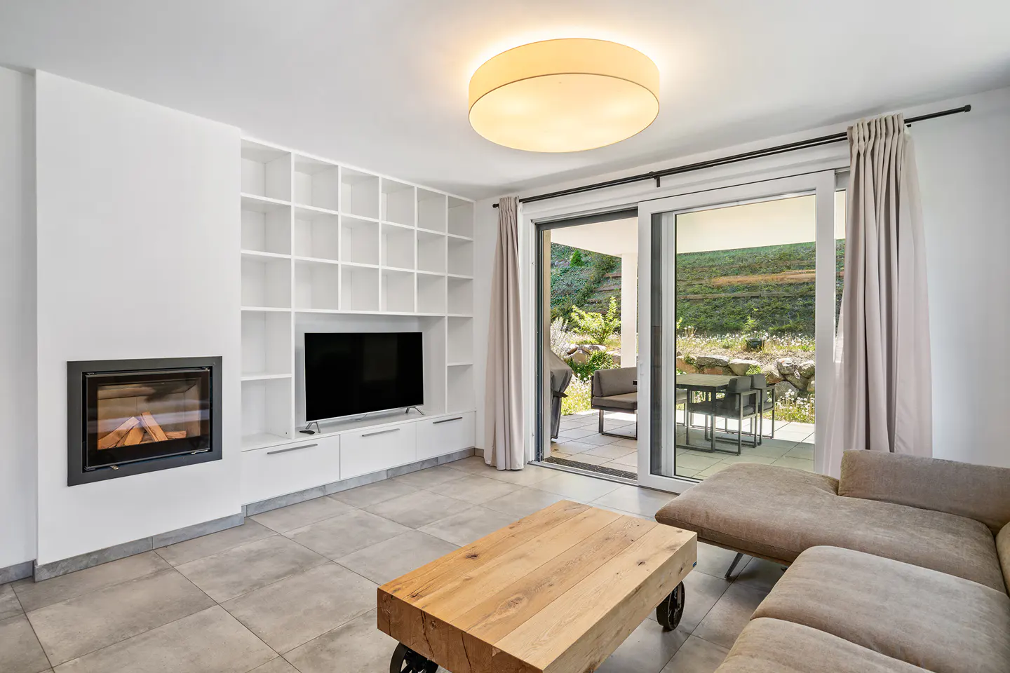 Bright living room with a fireplace, TV, and built-in shelves. Sliding glass doors open to a patio with outdoor seating.